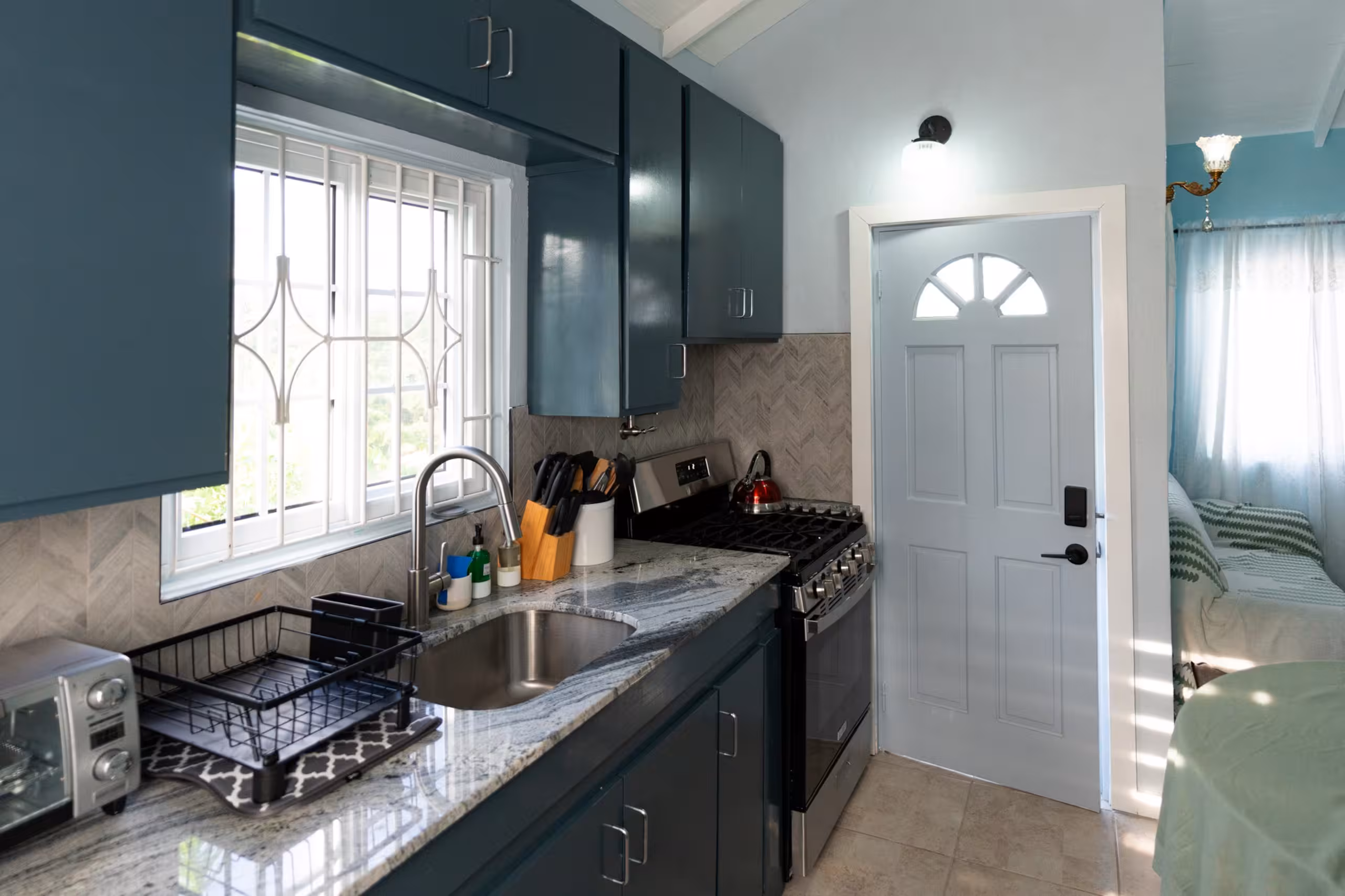 Clean kitchen with blue cabinets, sink, stove, and window light